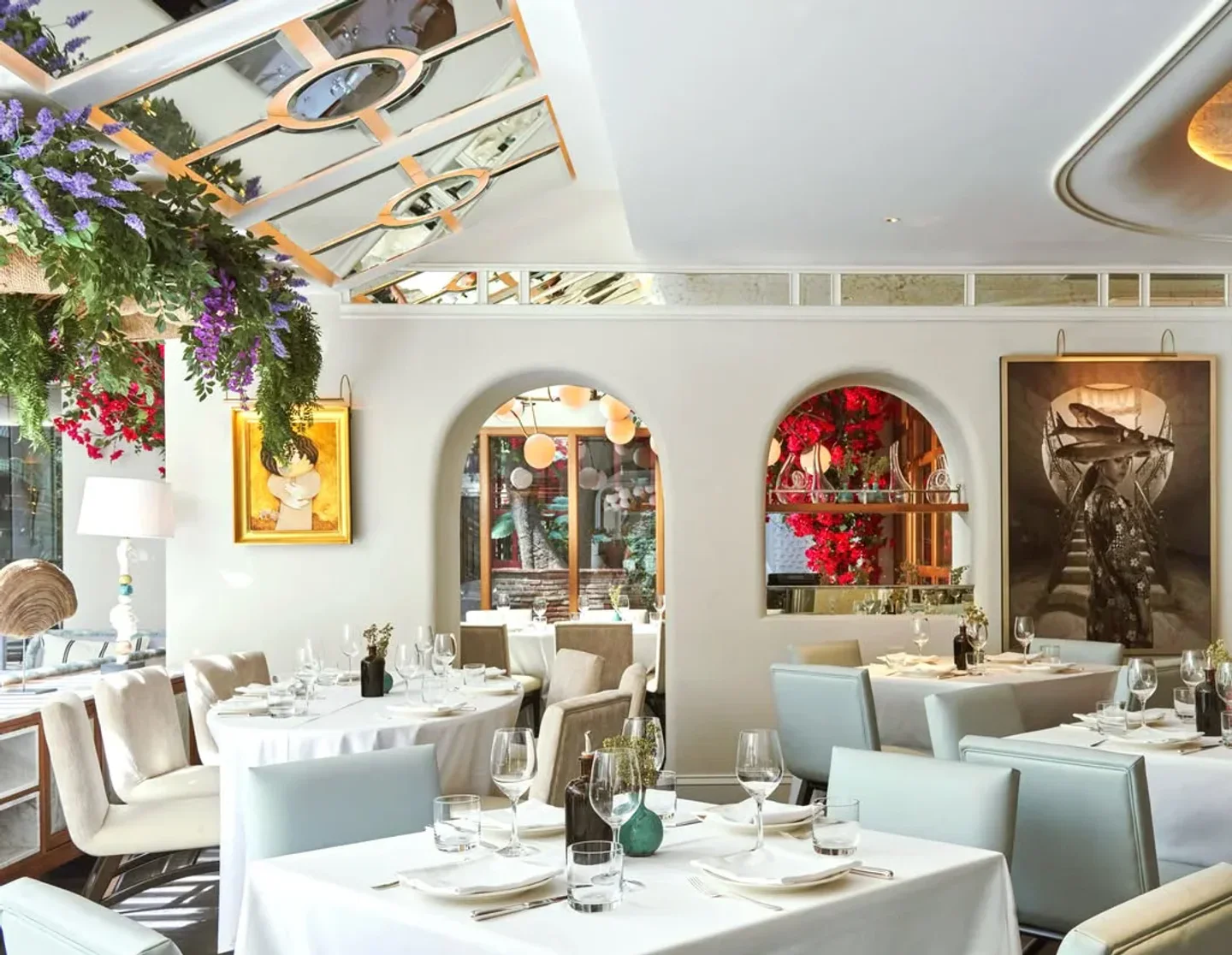 Elegant dining room at GAIA restaurant in Marbella, featuring white tablecloths, plush seating, and artistic wall decor.