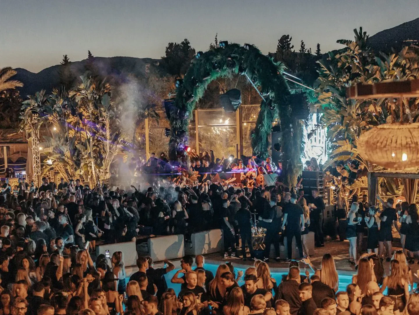 Nightclub crowd at Nao Marbella with palm trees and a lively dance floor.