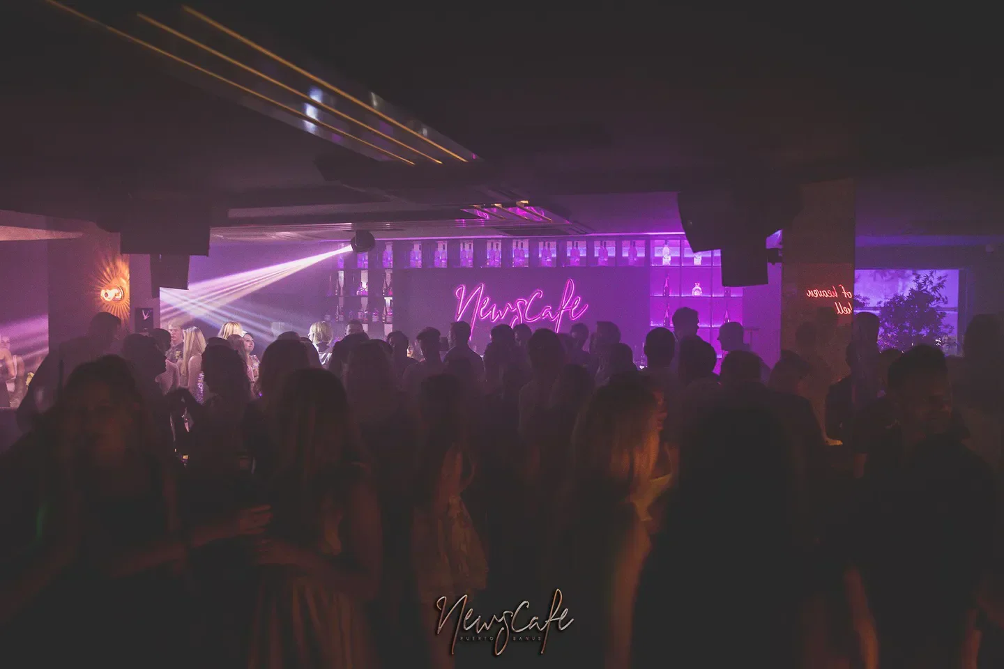 News Cafe nightclub in Marbella, a vibrant scene with neon lights and a crowd.