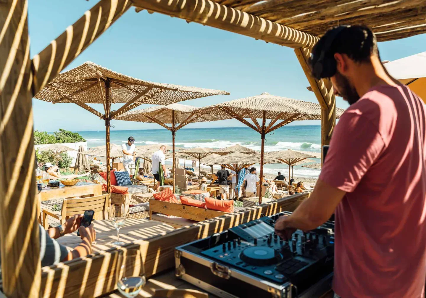 DJ playing music at Nosso Beach Club in Marbella, with beach umbrellas and ocean views.