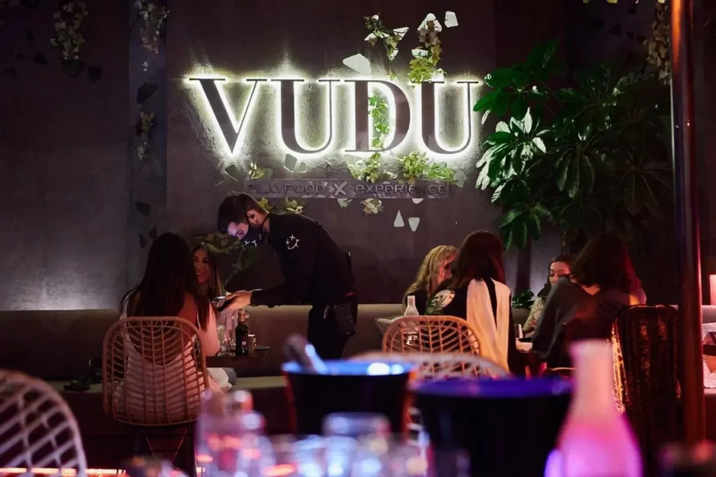 Inside Vudu restaurant in Marbella, with the illuminated logo and customers being served.